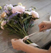 En person binder en bukett med blommor med ett band på ett bord.